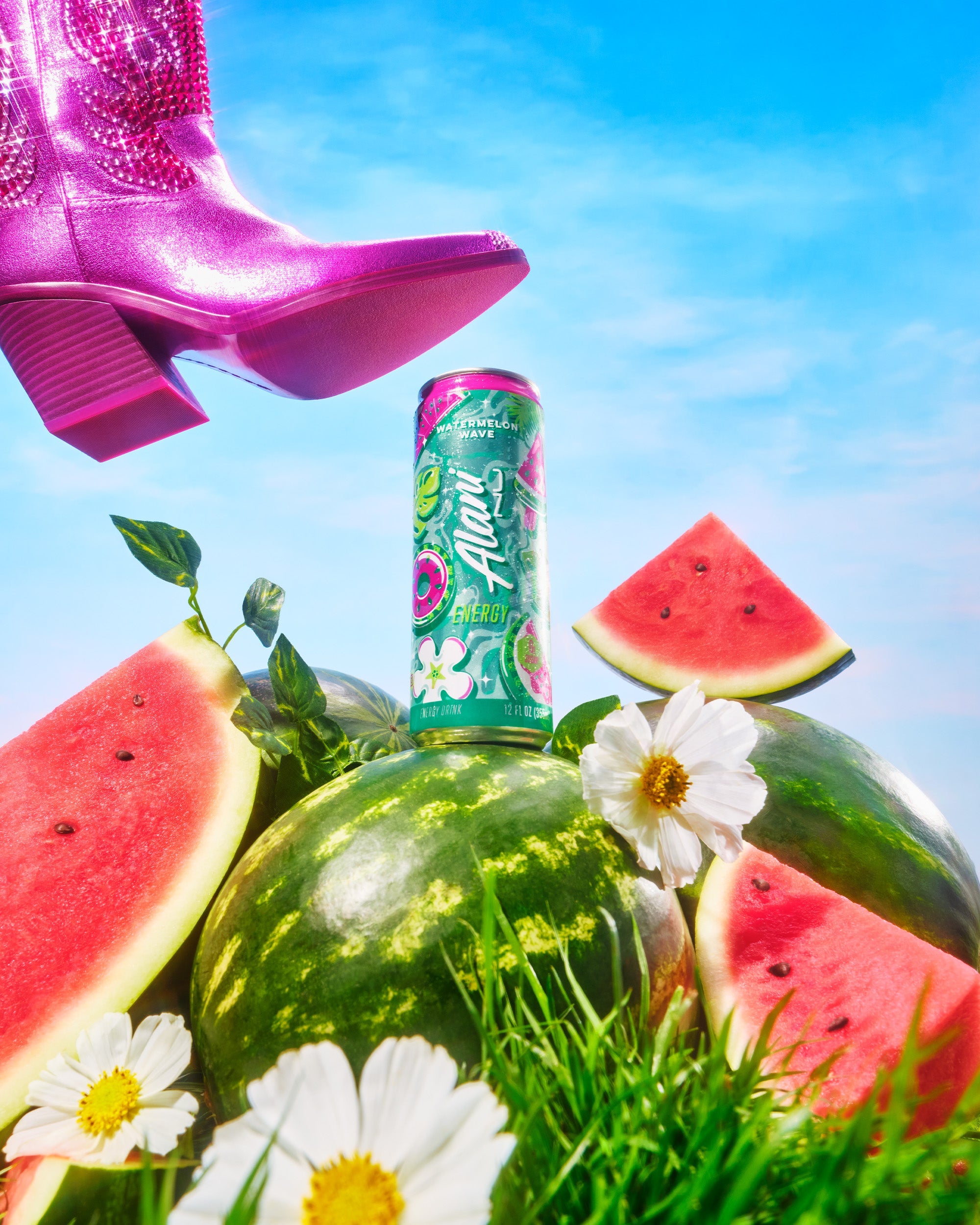 A can of Alani Nu Watermelon Wave Energy sitting atop a whole watermelon in a plot of grass surrounded by sliced watermelon, flowers, and vines. A pink cowboy boot is just above the can as if it’s going to smash it.